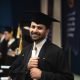 A proud male graduate holding his diploma in a cap and gown during a ceremony in Baghdad, Iraq.